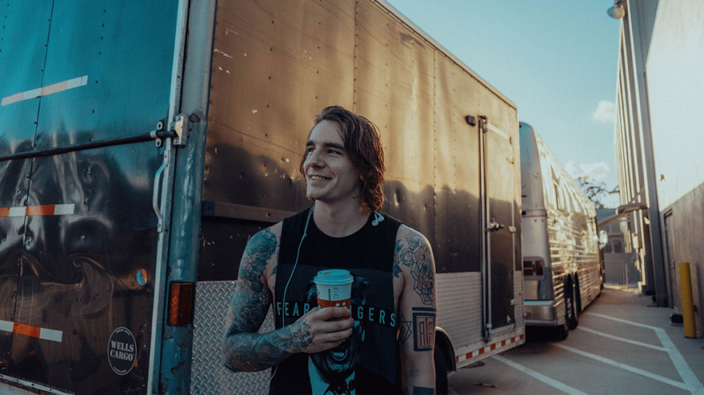Man with tattoos standing next to a tour bus